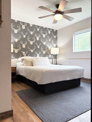 Une chambre à coucher avec un lit, un ventilateur de plafond, une lampe fixée au mur et une fenêtre.