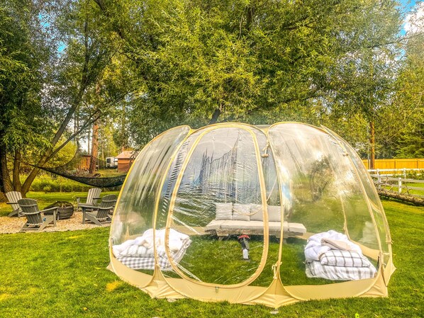 Deux tentes transparentes, avec un hamac et des chaises, installées dans un espace herbeux.
