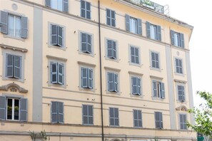 Un edificio de varios pisos con ventanas y contraventanas uniformes, que presenta una fachada simétrica y un balcón en el piso superior.