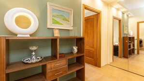A well-lit hallway with a wooden console table displaying a decorative plate, a framed painting, and a small vase. A wooden door and a mirror are also visible. - Casa Prati apartment (Rome)