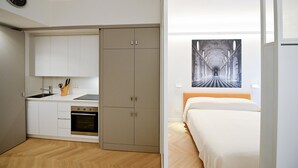 A compact room with a kitchenette, a bed, and a large framed artwork on the wall.