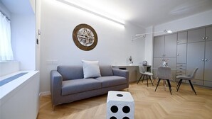 A modern living room with a grey sofa, a round wall art piece, a dining table with chairs, and a grey wardrobe.