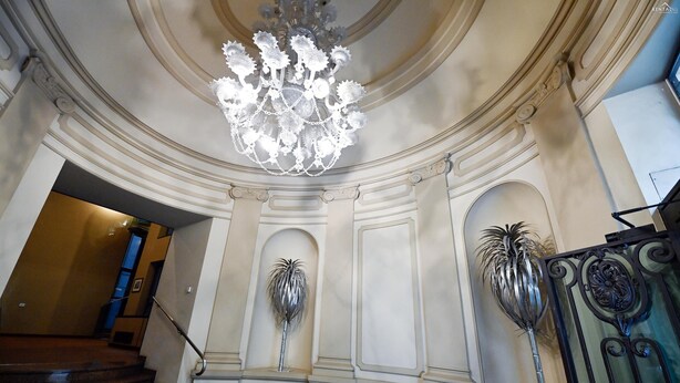 A grand staircase with a chandelier, ornate wall decorations, and a metal gate.