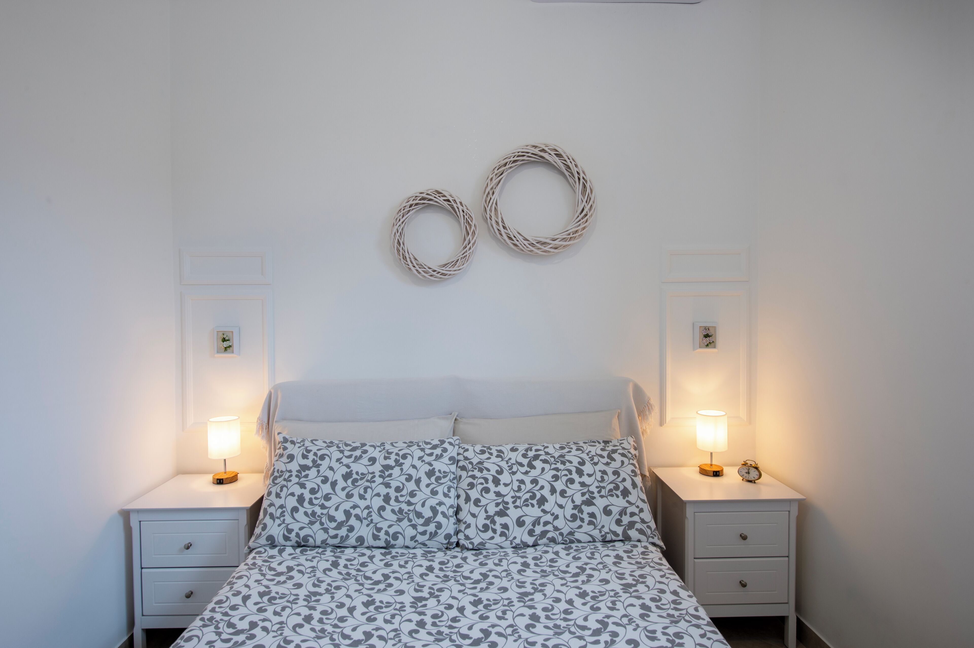 Une chambre à coucher comprenant un lit, deux tables de chevet, deux lampes fixées au mur et deux éléments de décoration murale.