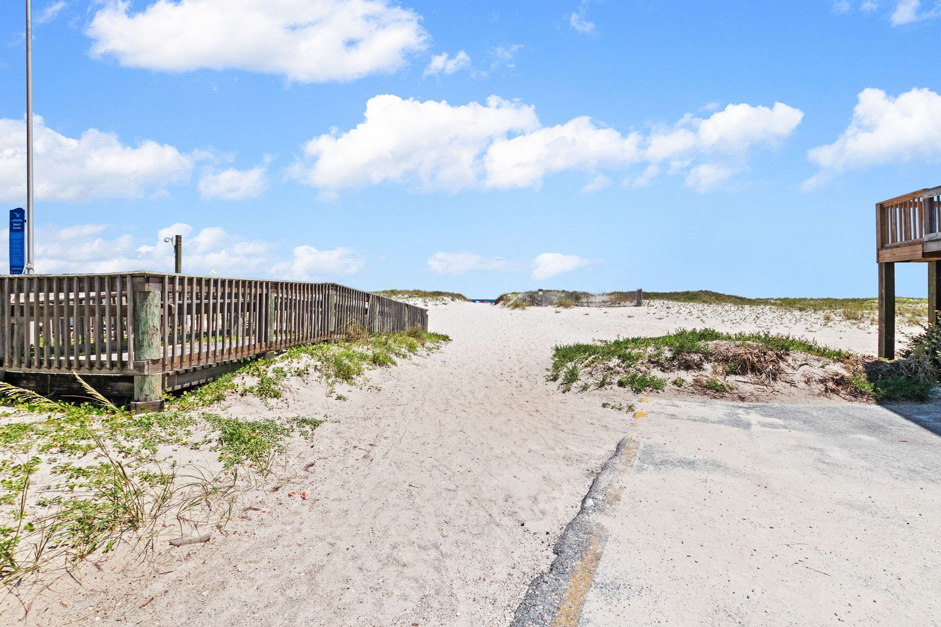 A sandy beach path with wooden railings and a wooden structure on the right.