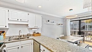 A modern kitchen with white cabinetry, granite countertops, and a large window overlooking a balcony. - 2BR Condo Beach Access Pool and Walk to Hangout (Gulf Shores)