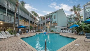 A pool area with lounge chairs and umbrellas, surrounded by multi-story buildings with balconies. - 2BR Condo Beach Access Pool and Walk to Hangout (Gulf Shores)