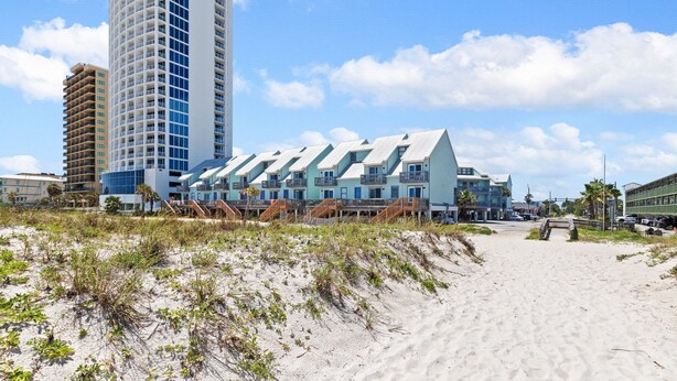 A beachfront hotel with a modern design, featuring a prominent tower and a series of connected buildings with balconies. - 2BR Condo Beach Access Pool and Walk to Hangout (Gulf Shores)