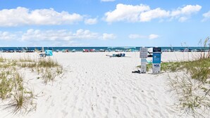A beach with white sand, a few umbrellas, and a signboard. - 2BR Condo Beach Access Pool and Walk to Hangout (Gulf Shores)