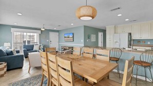 A spacious living room with a wooden dining table, blue sofas, and a kitchen area with white cabinets. - Spacious 3BR 2BA Gulf Views Dock and Boat Launch (Gulf Shores)