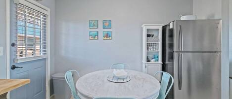 Una cocina compacta con una mesa redonda, sillas azul claro, un refrigerador de acero inoxidable y un mueble pequeño.