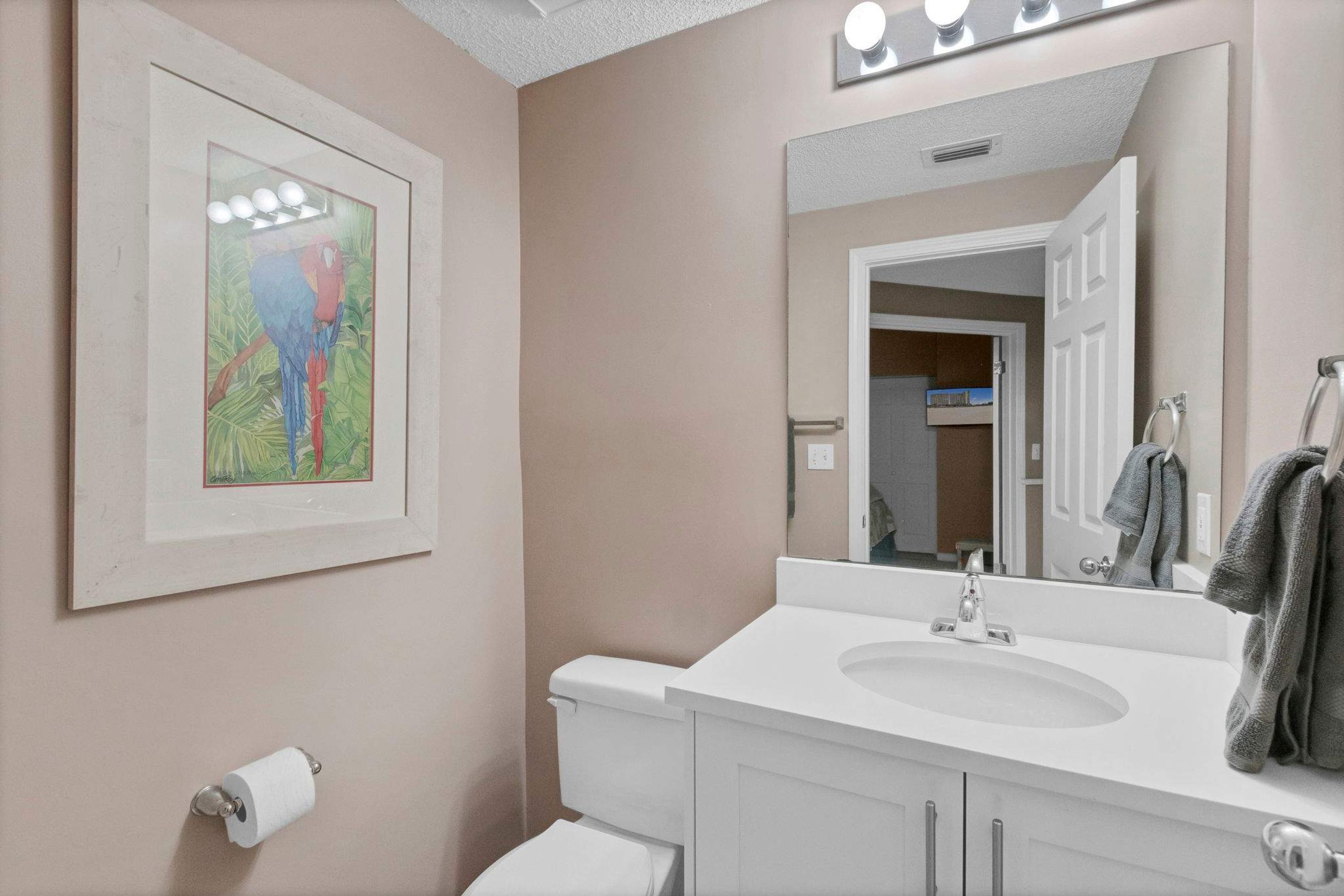 A bathroom with a white sink, mirror, and toilet. There is a framed picture on the wall and a towel rack with towels.