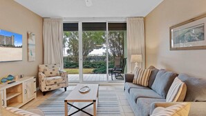 Un salon comprenant un canapé, un fauteuil, une table basse et donnant sur un balcon aménagé avec du mobilier d’extérieur.