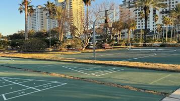 Una cancha de baloncesto con aro, rodeada de palmeras y edificios.