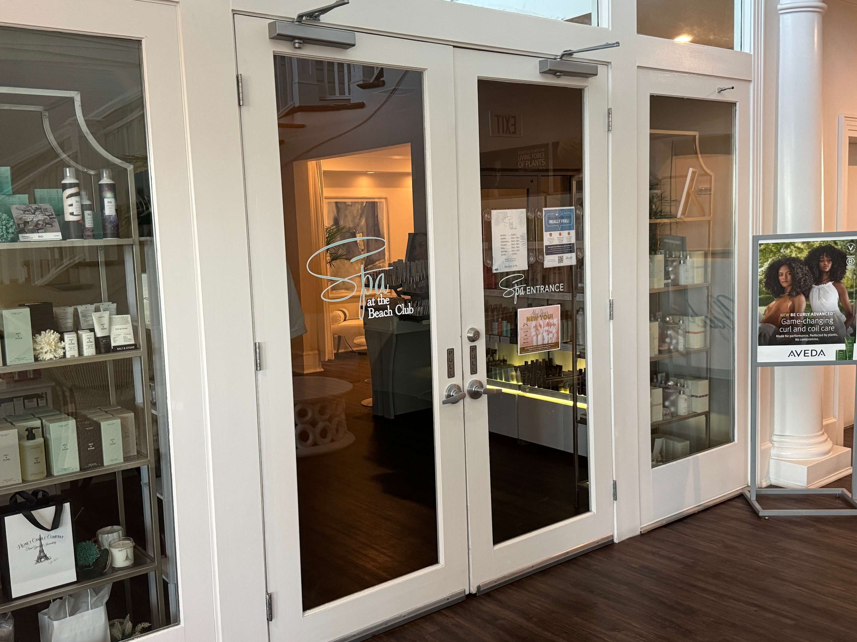 A spa entrance with glass doors, a sign for 'Spa at the Beach Club', and a display of spa products.