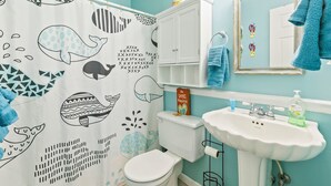 Baño con inodoro y lavamanos blancos, y cortina de ducha con estampados de ballenas y motivos geométricos.
