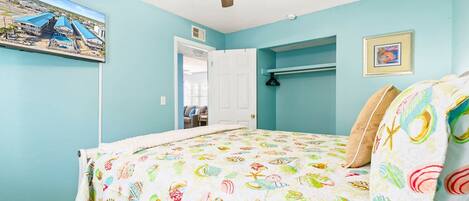 Un dormitorio con cama, ventilador de techo, puerta y televisor montado en la pared.