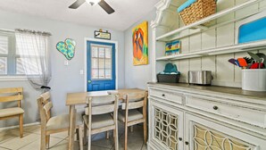 Una cocina con puerta azul, sillas de madera, un armario blanco y un ventilador de techo.