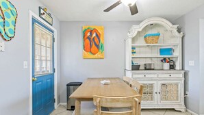 Un comedor con una mesa y sillas de madera, una puerta azul y un armario blanco con estantes.