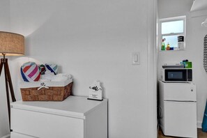 A small kitchenette with a microwave and refrigerator, a wicker basket with towels, and a lamp. - Waves on Desoto Studio With Pool 3 (Hollywood)