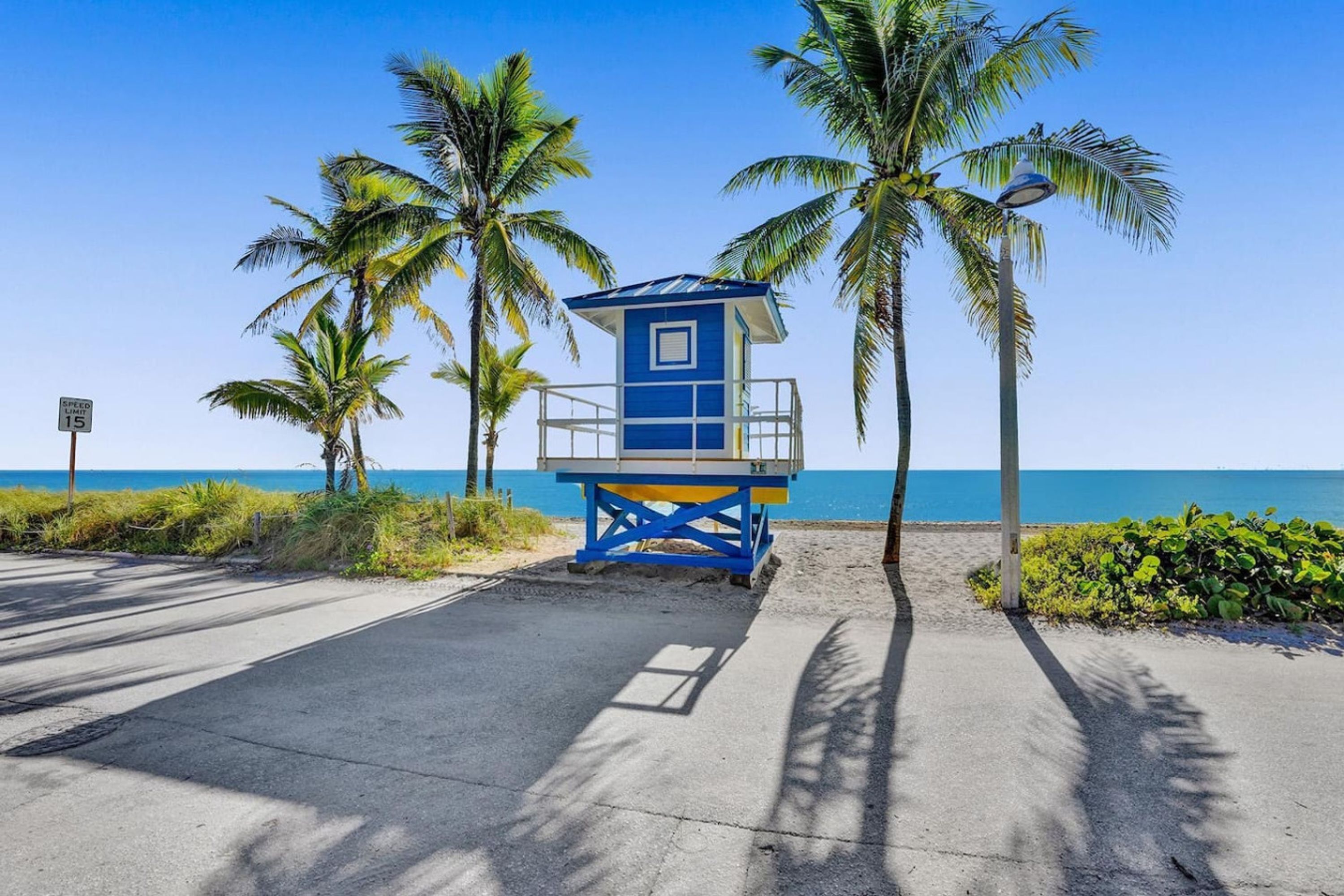 A lifeguard tower with a blue and yellow color scheme, surrounded by palm trees and a clear view of the ocean.