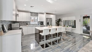 A modern kitchen with a marble floor, white cabinetry, and a central island with bar stools. - Daddy House-victoria Park With Pool (Fort Lauderdale)
