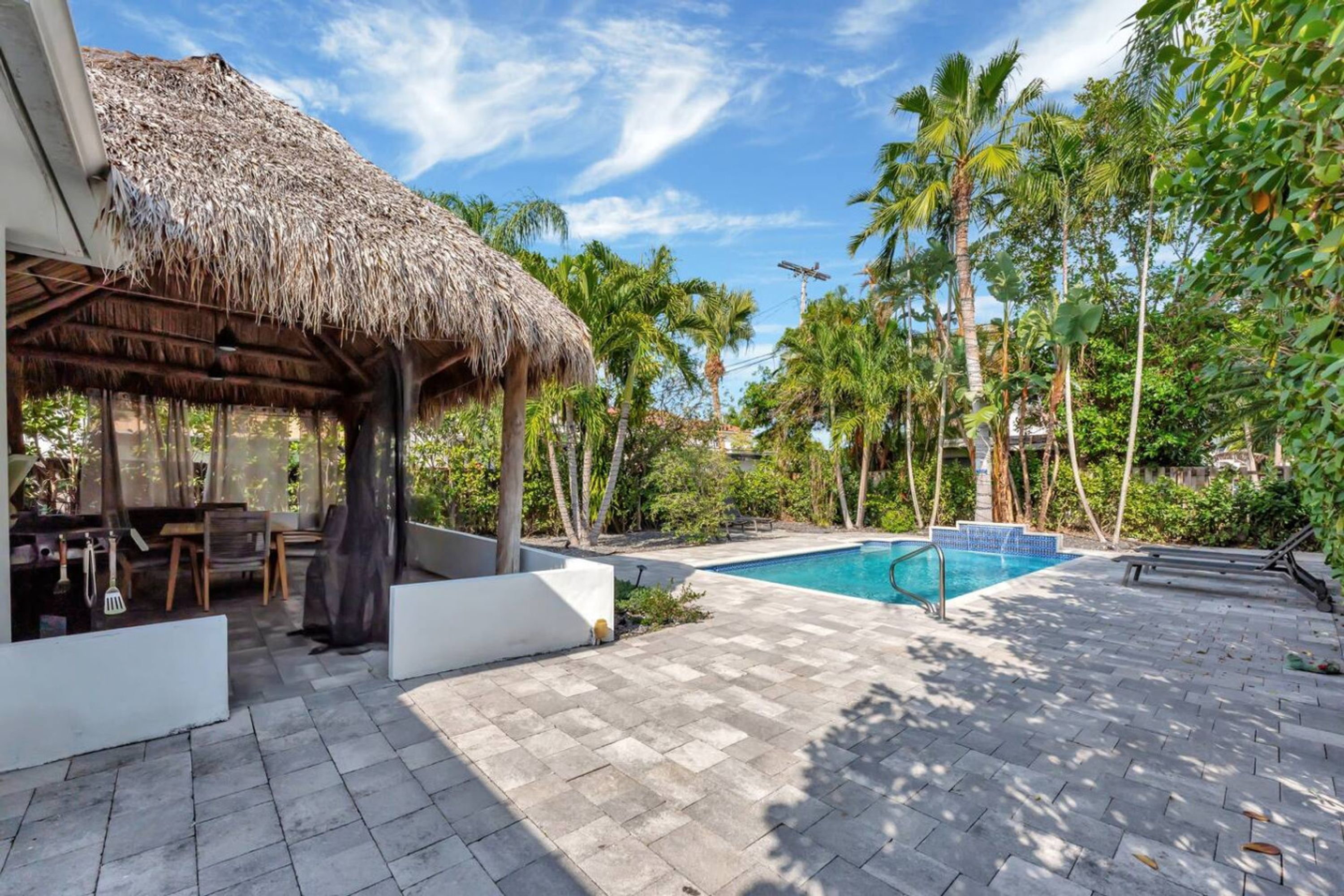A pool area with a thatched-roof structure, palm trees, and a tiled patio.