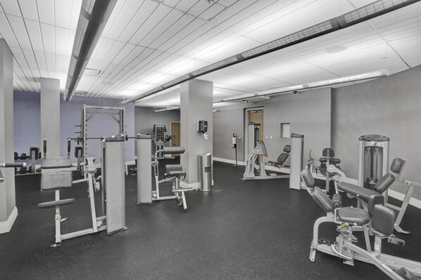 A gym with various exercise machines, a large mirror, and a door leading to another room.