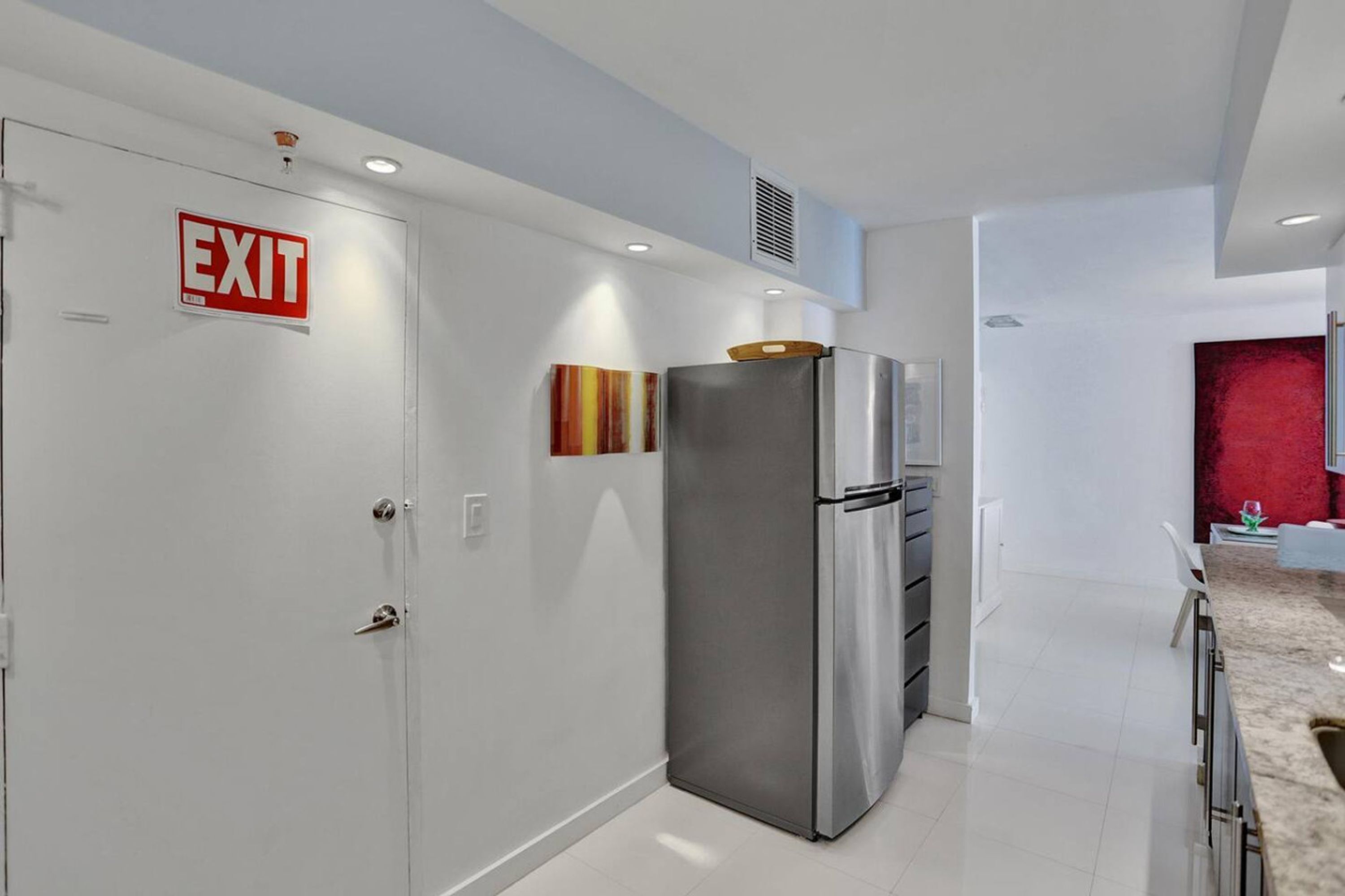 A modern kitchen with a stainless steel refrigerator, an exit sign, and a red accent wall.
