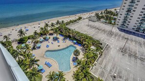 A resort with a swimming pool surrounded by palm trees and beach chairs, overlooking a beach and ocean. - Beautiful 1 1 Beach View 14 Floor (Hollywood)