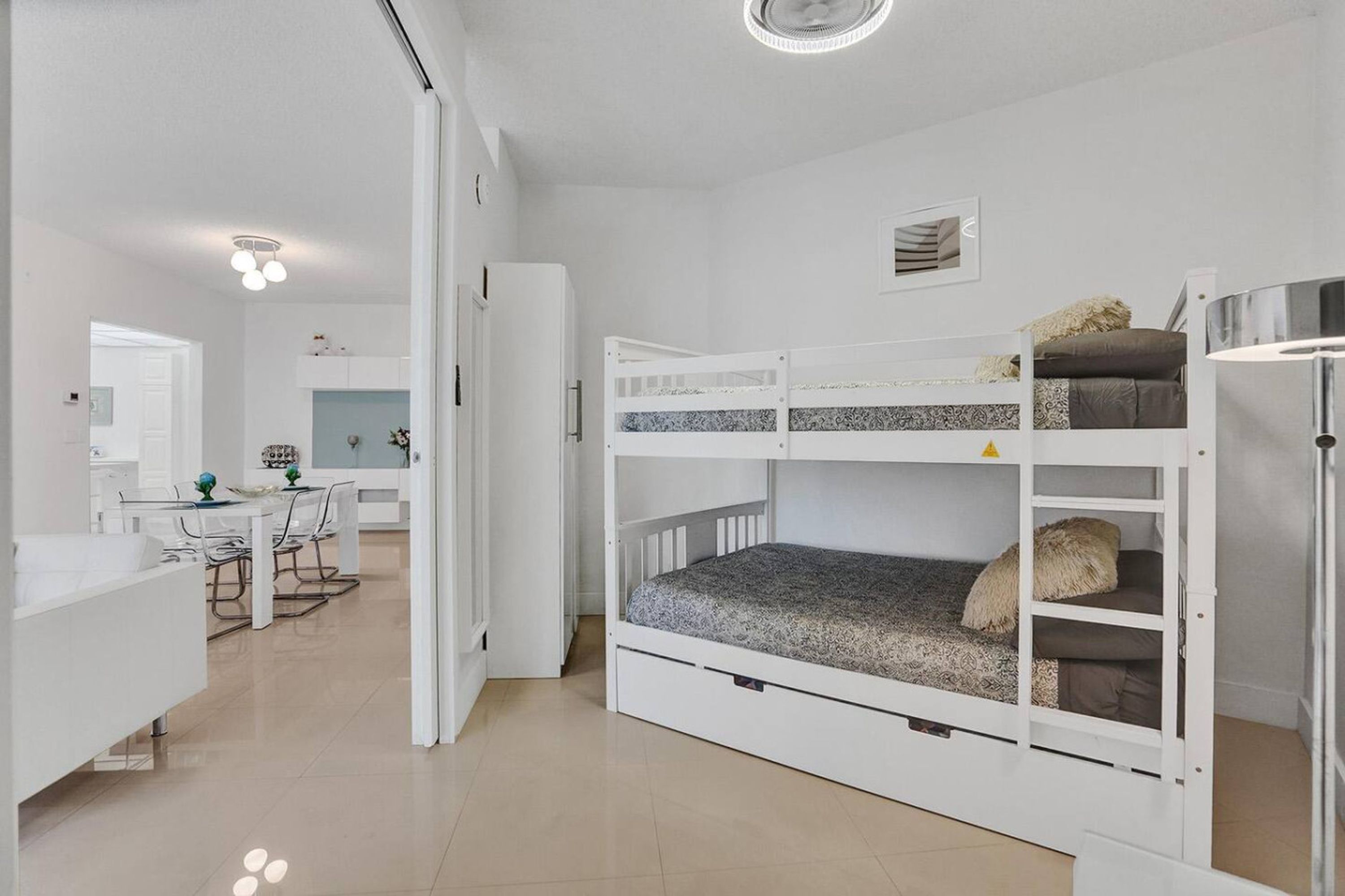 Ein Zimmer mit einem Etagenbett, einem Schreibtisch und einem Stuhl. Eine Tür führt in ein weiteres Zimmer.