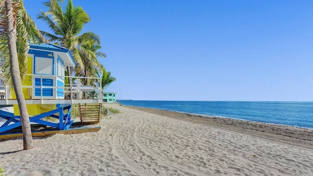 A beach with a lifeguard tower, palm trees, and a clear blue sky. - Waves on Desoto Beautiful Studio 8 (Hollywood)