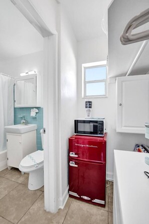 A compact bathroom with a white toilet, a sink, a red cabinet, a microwave, and a window.