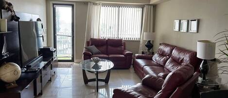 Una sala de estar con un sofá de cuero rojo, una mesa de centro de vidrio y un televisor sobre un mueble bajo.
