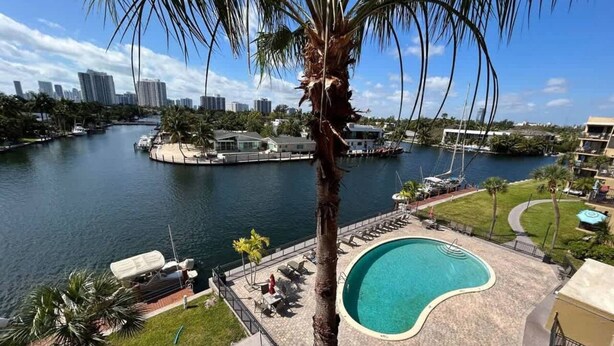 A view of a waterfront property with a swimming pool, palm trees, and a marina in the background. - Beautiful Water View Golden Isles (Hallandale Beach)
