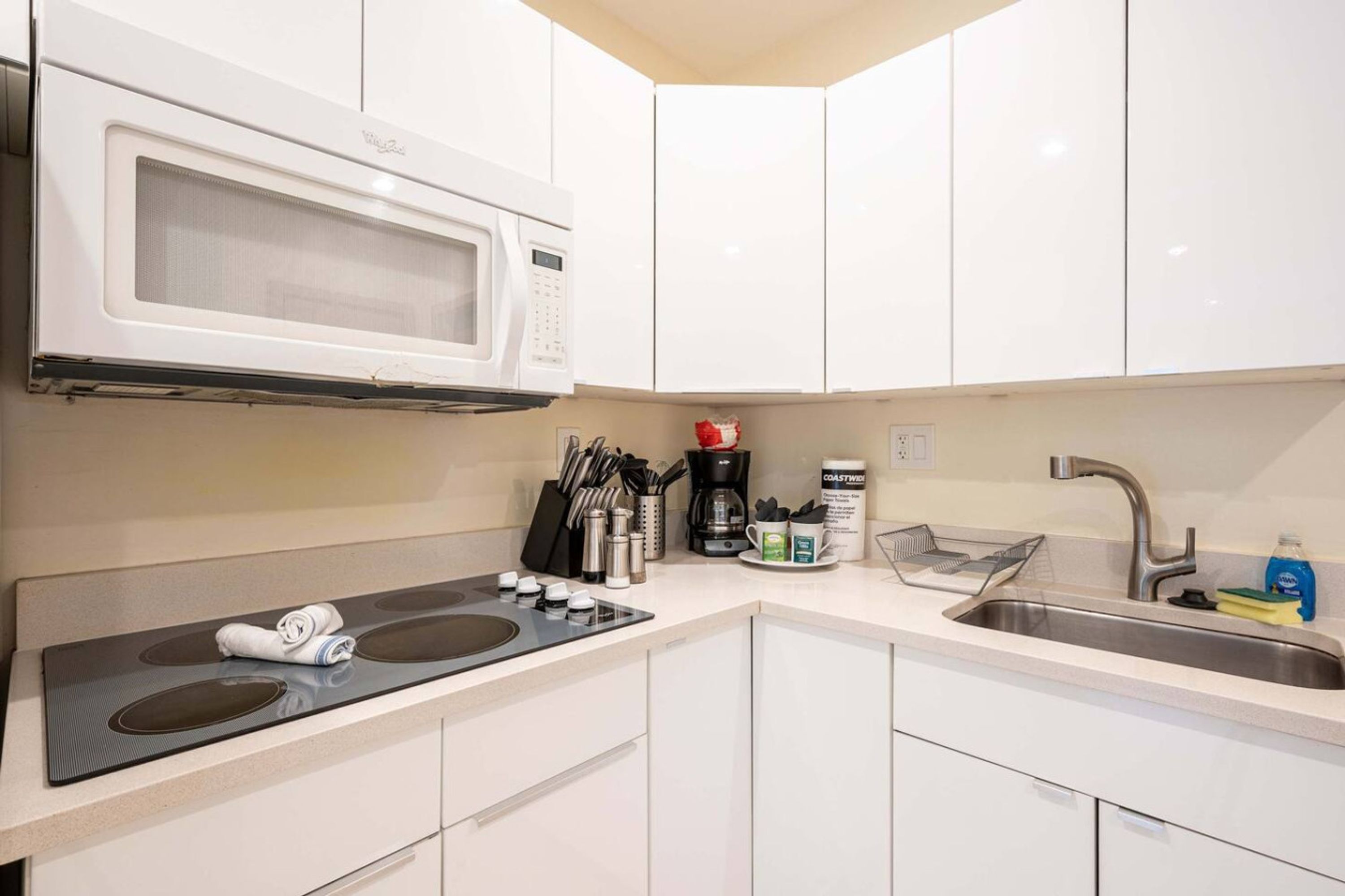 A modern kitchen with white cabinets, a built-in microwave, a stove, and a sink.