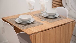 Una mesa de comedor con platos blancos, cuencos y copas de vino, servida con individuales.