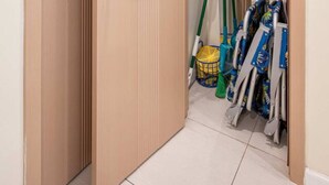 Un armario de madera con repisas y una barra para colgar, que contiene productos de limpieza y una cesta.