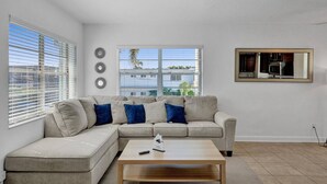 A modern living room with a sectional sofa, a coffee table, and a large window with blinds.