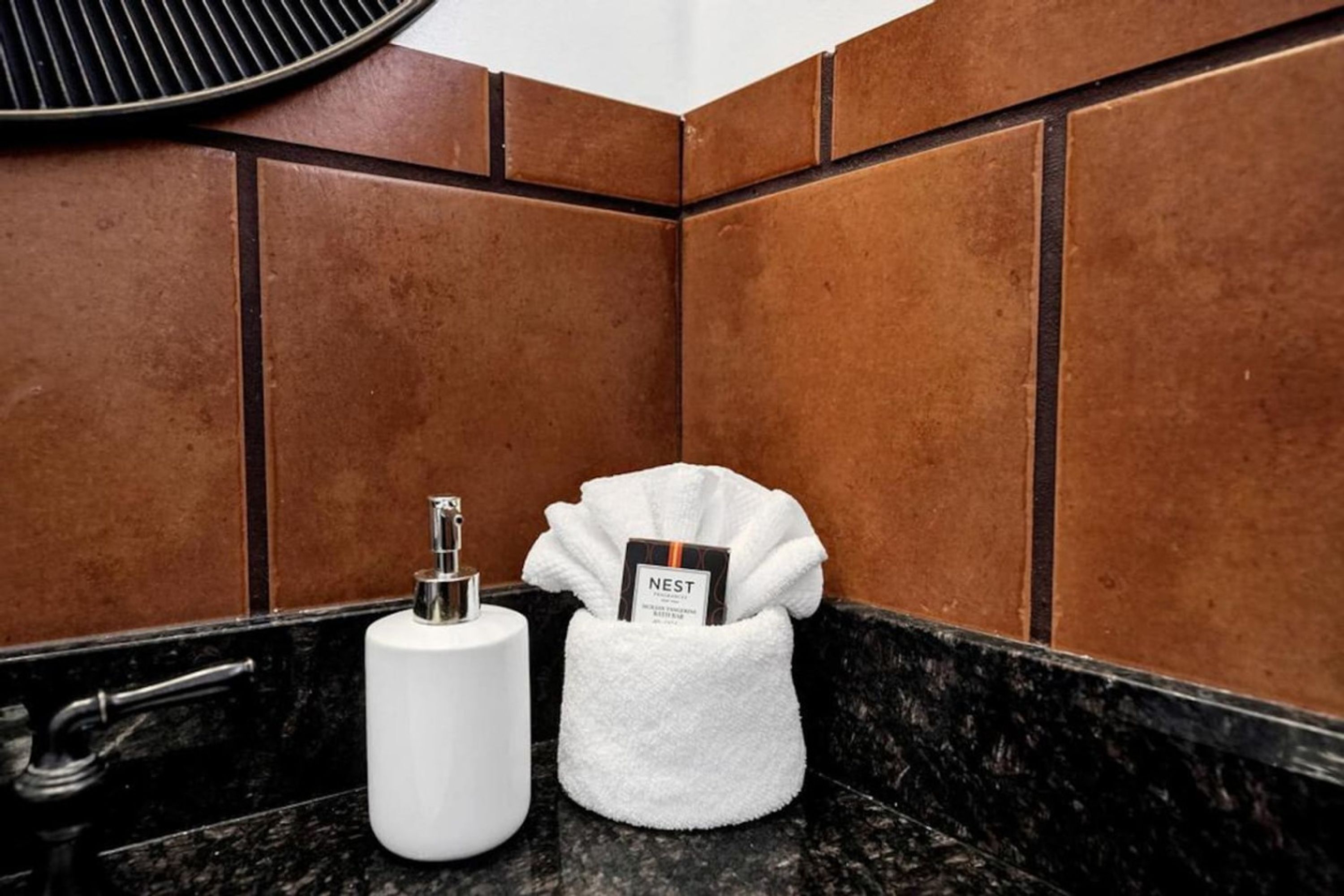 A bathroom with a black marble countertop, a white sink, and a towel dispenser with a branded card.