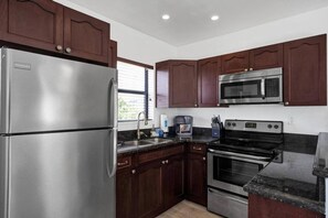 A kitchen with dark wooden cabinets, stainless steel appliances including a refrigerator, microwave, and oven, and a granite countertop. - Waves On Walnut 4-beach Access (Hollywood)