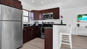 A modern kitchen with dark wood cabinets, stainless steel appliances, and a white island with seating. - Waves On Walnut 4-beach Access (Hollywood)