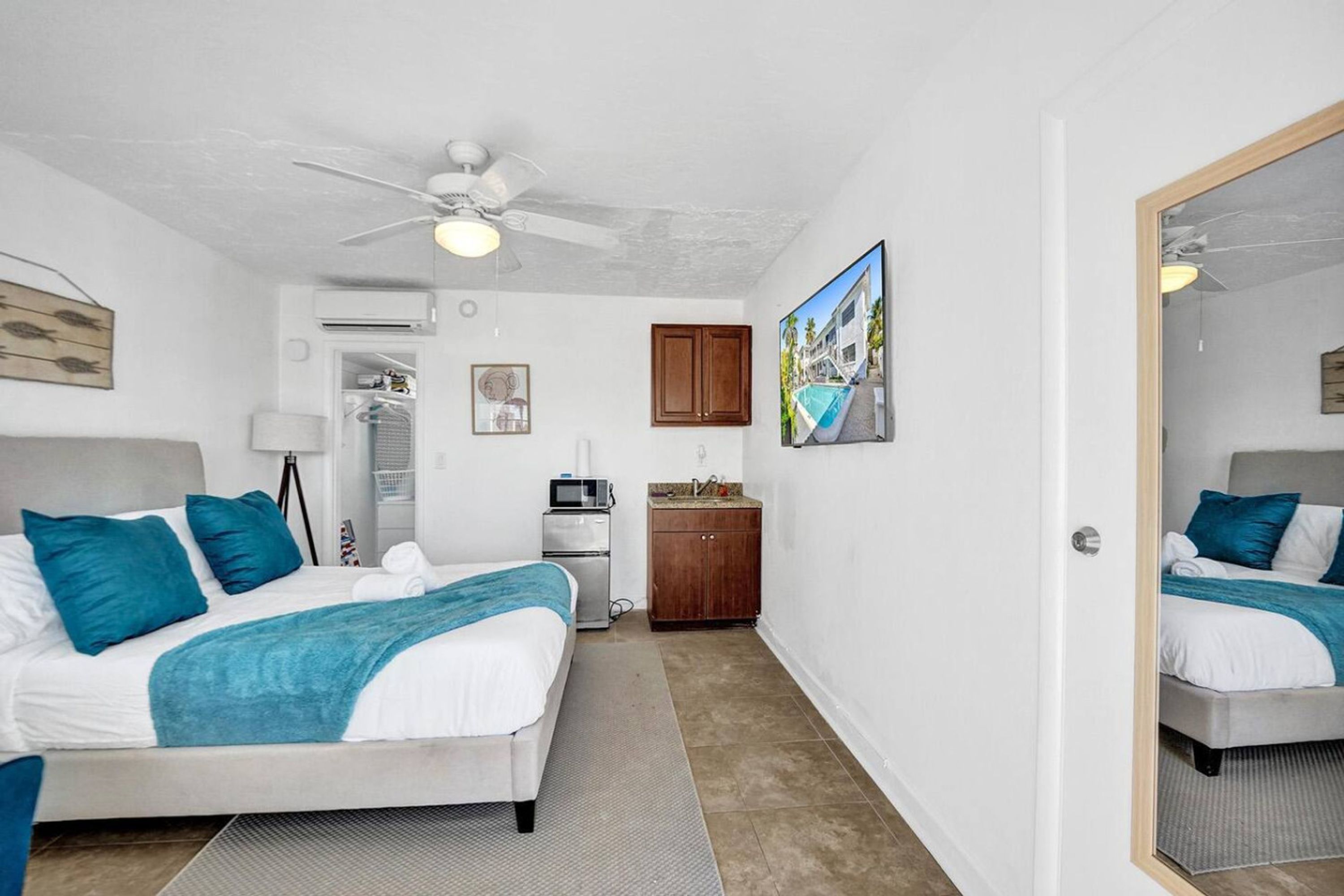 A hotel room with a bed, a ceiling fan, a small kitchenette, and a bathroom.