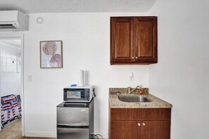 A kitchen with a stainless steel refrigerator, a microwave, and a sink with granite countertop. There is a wooden cabinet above the sink and a framed picture on the wall. - Waves on Desoto Beautiful Studio 7 (Hollywood)