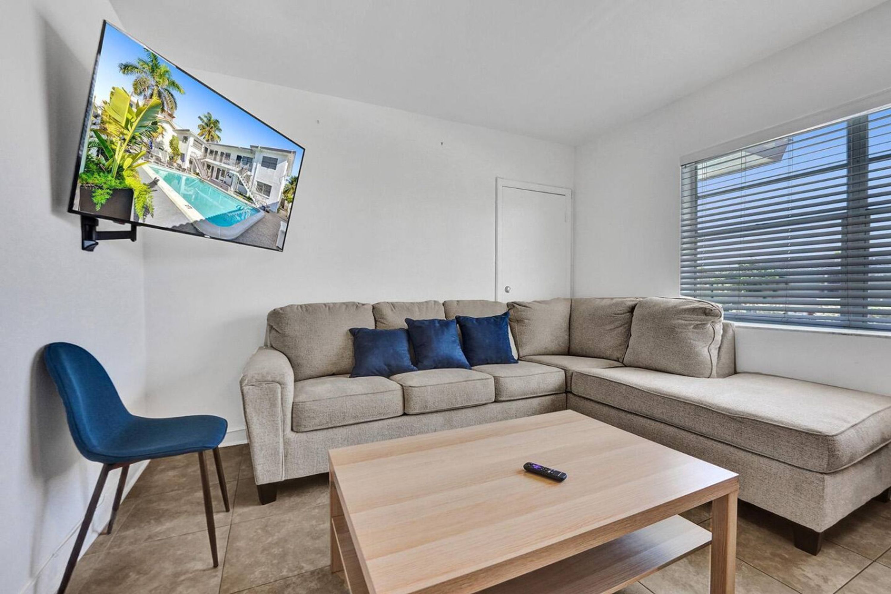 A modern living room with a sectional sofa, a blue chair, a coffee table, and a flat-screen TV mounted on the wall.