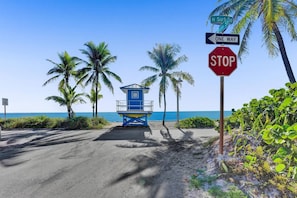 Een strand met een bewakershutje, palmbomen en een stopbord.