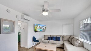 Un salon moderne avec un canapé beige, une table basse, un téléviseur fixé au mur et un ventilateur de plafond.