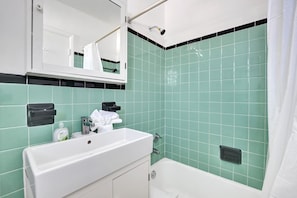 Een badkamer met een wit wastafelmeubel, een spiegel en een douchegedeelte met groene tegels.