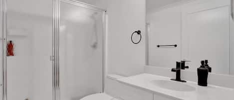 Ein Badezimmer mit Glasdusche, weißer Toilette und Waschtisch mit Spiegel.