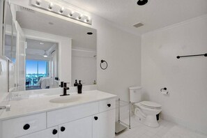 Un baño moderno con tocador blanco, un espejo grande y un inodoro.